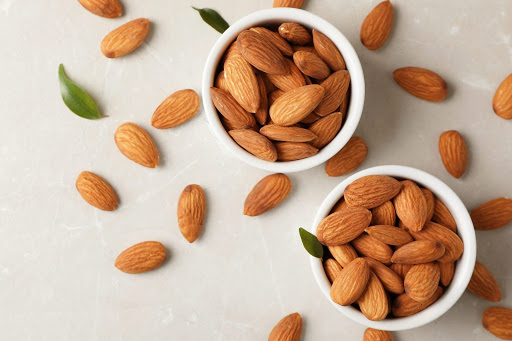 Tasty organic almond nuts in bowls and space for text on table, top view